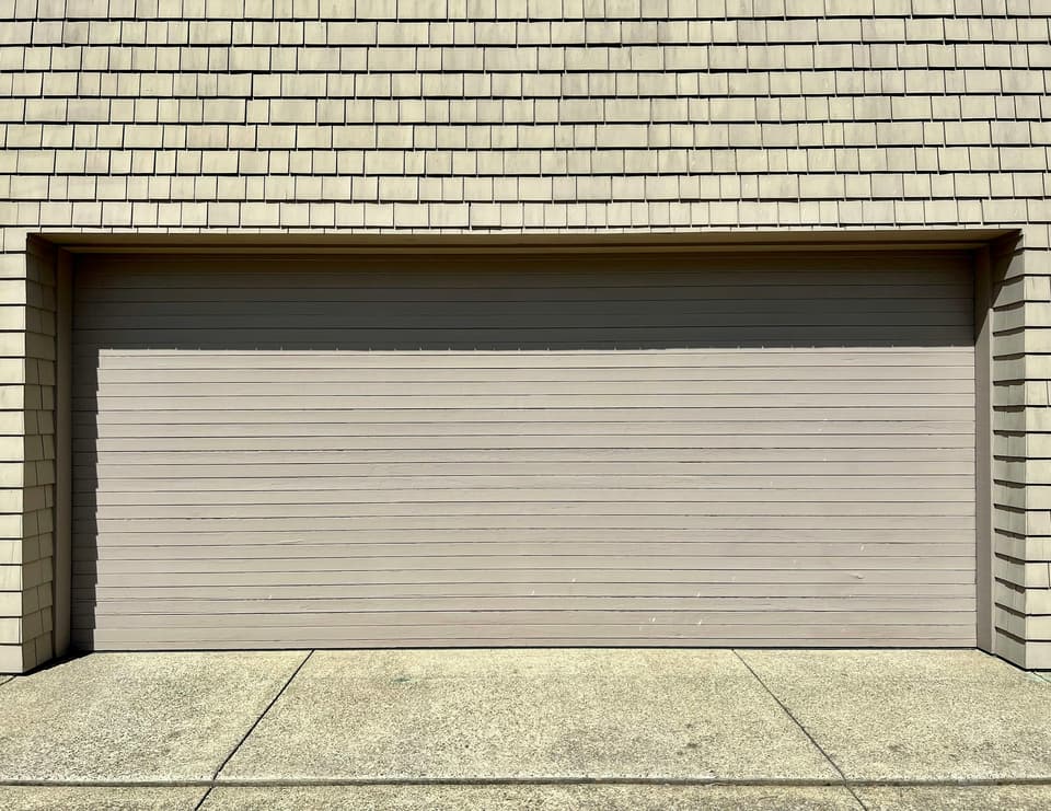 A wide double garage door on a shingle-sided house